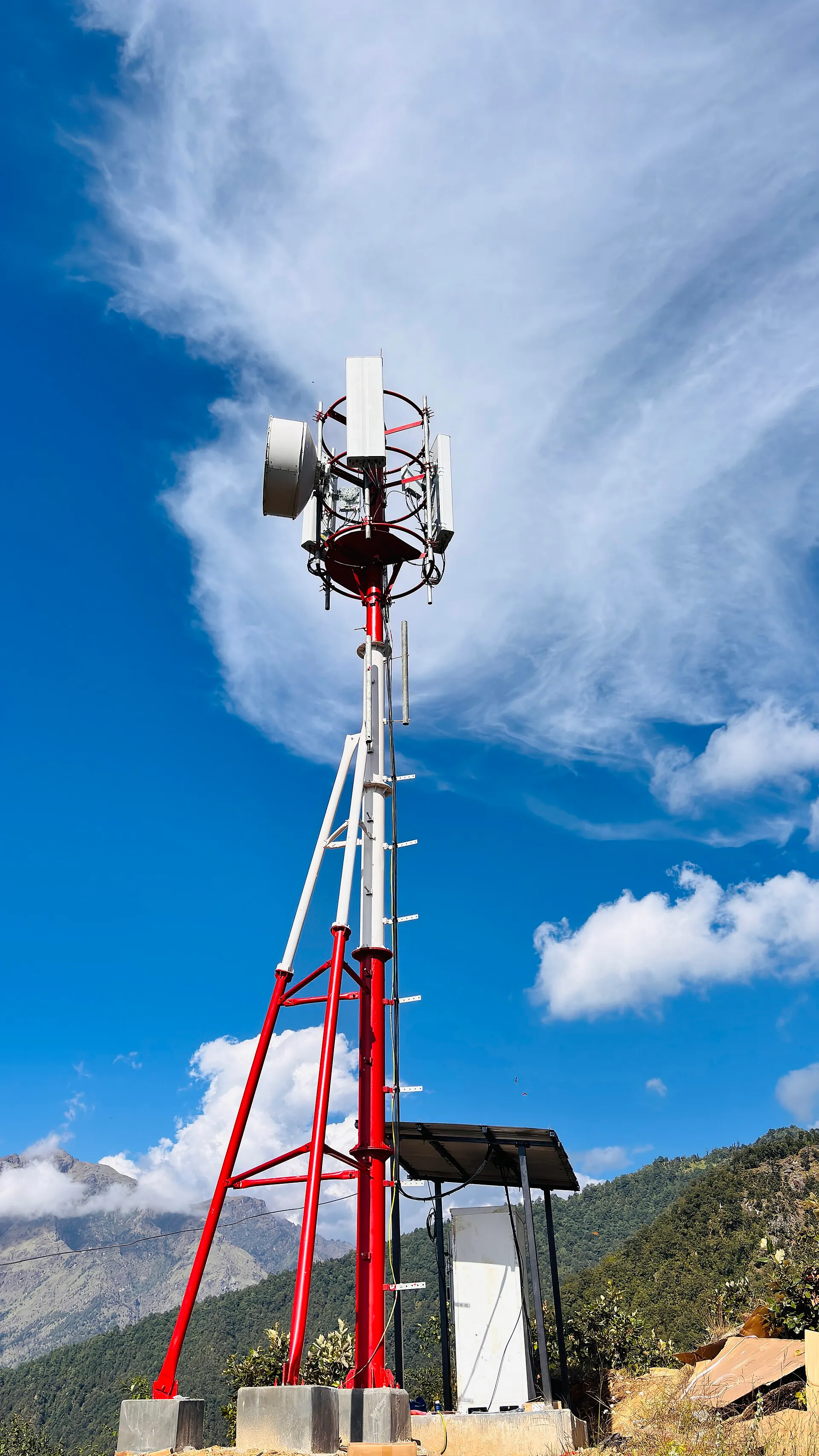 Red and white mobile network mast with antennas on a hillside in Nepal