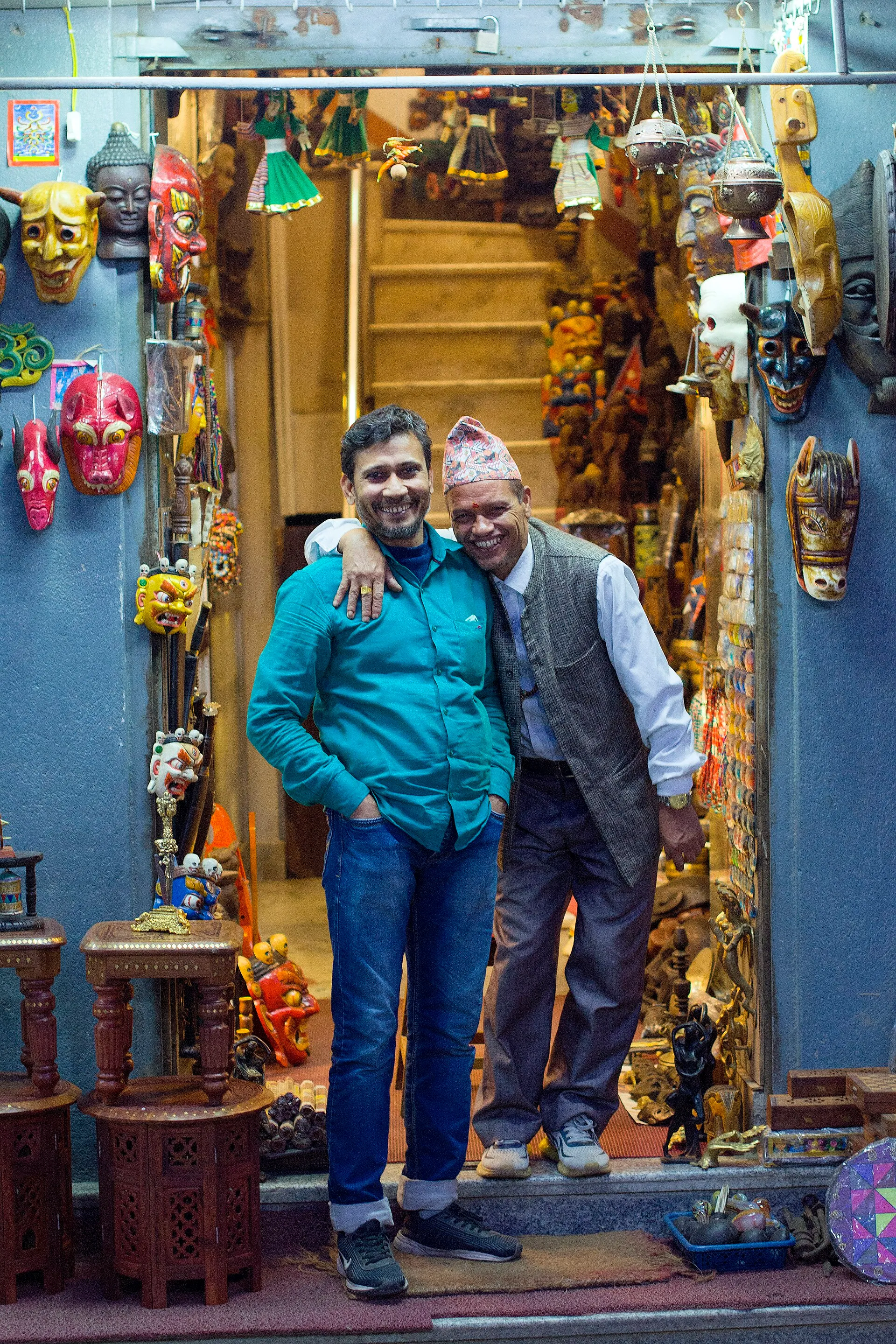 Two shopkeepers standing together at the door of a Kathmandu handicraft shop with masks on the walls